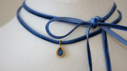 Blue choker necklace with a gold pendant on a mannequin.