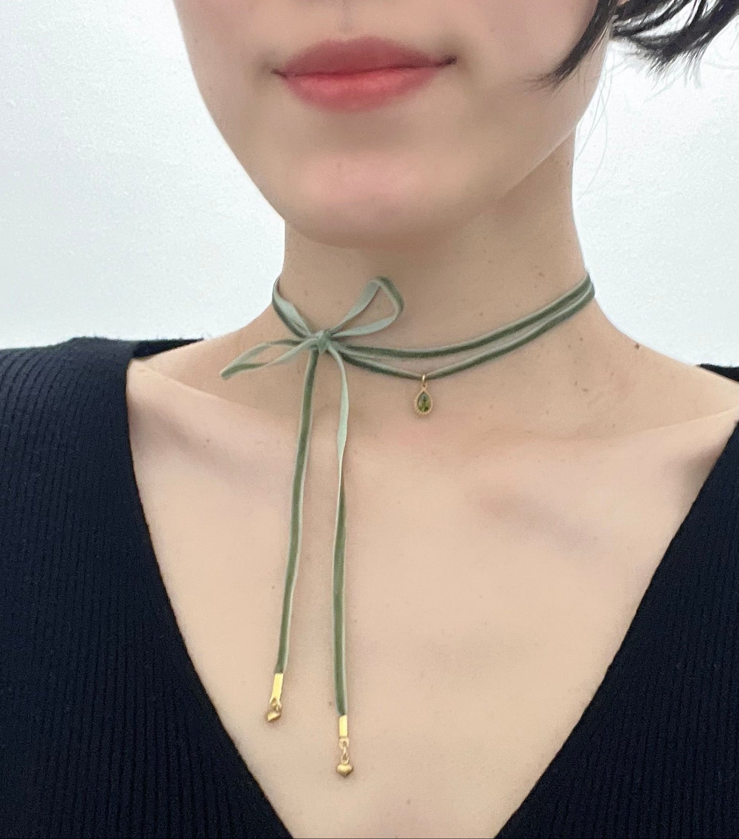 Green choker necklace with gold accents worn by a person on a plain background
