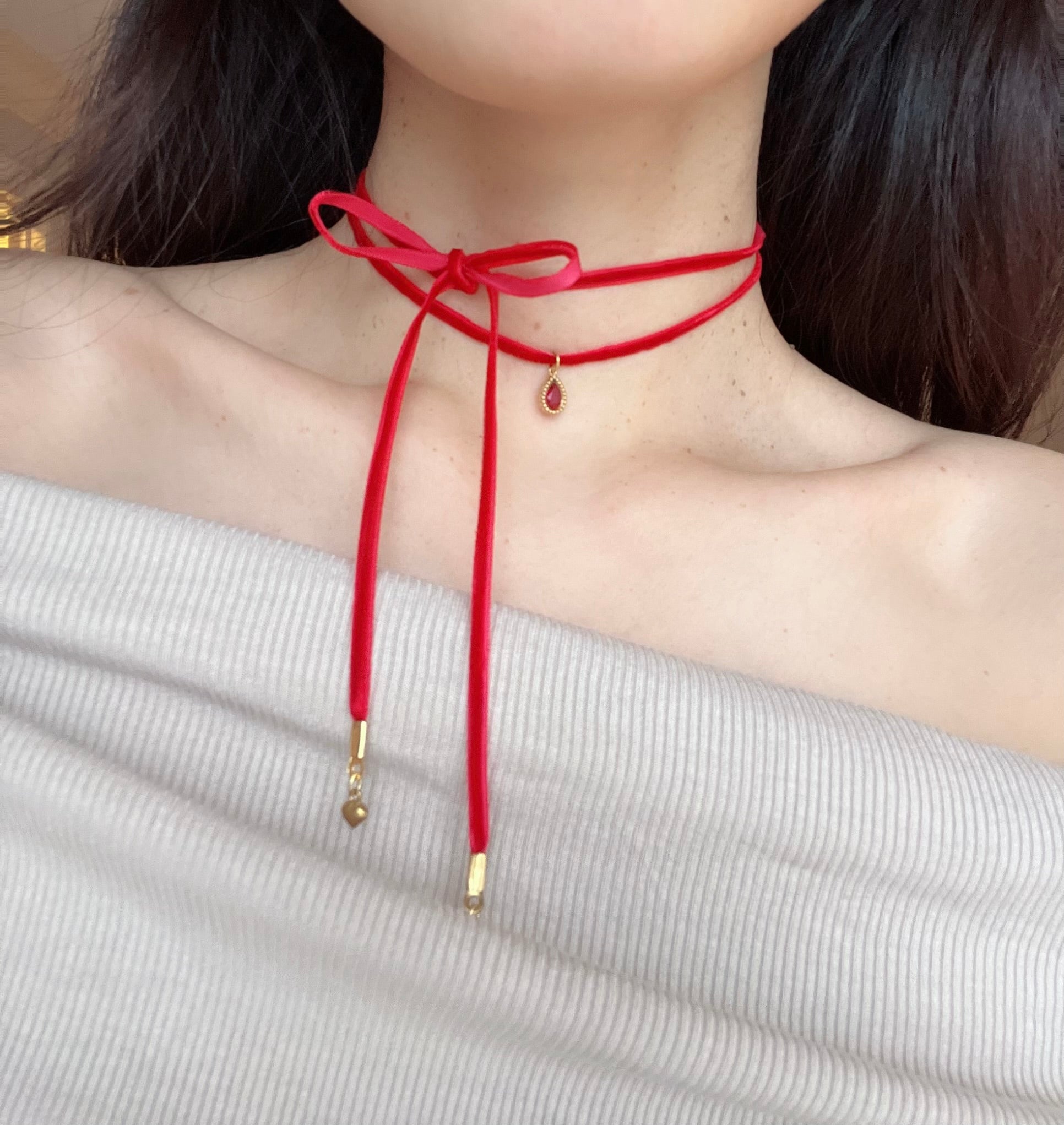 Red choker necklace with gold accents worn by a person against a neutral background