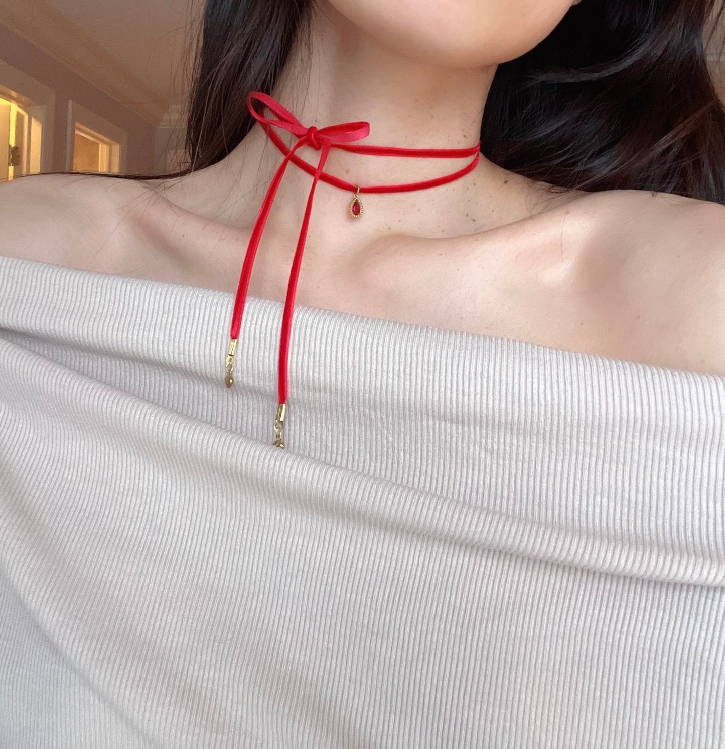 Person wearing a red choker necklace with a white off-shoulder top.